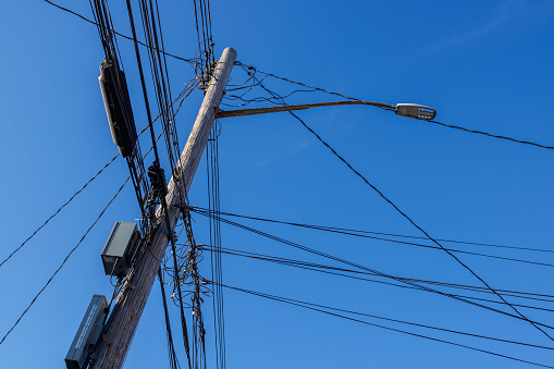 Messy internet and TV cables, phone lines, and electrical wires on a wooden telegraph pole against the blue sky on a sunny day. Queens, New York City, USA.