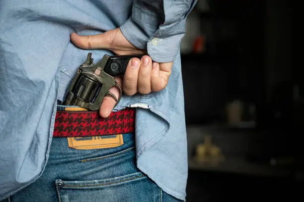 Photo of Personal weapons for self-defense. street crime concept. a man robs on the street. The search of the criminal, the man pulls a gun out of his jeans. Death threat.