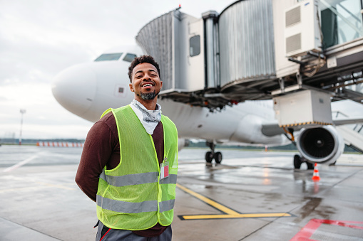 A joyful African-American airport worker posing in front of the plane.