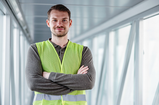 Portrait of a Caucasian airport worker standing proudly in the cabin, at the end of the loading bridge, and looking at the camera.