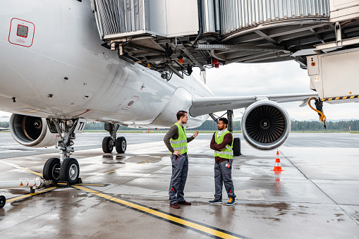Two aircraft engineers standing beside an airplane and communicating.