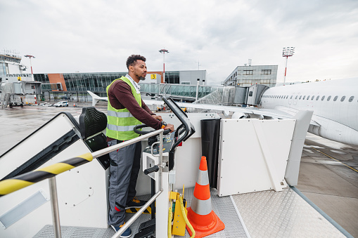 Portrait of an African-American male ground handling worker looking at the airplane. He is wearing a protective jacket. He manages the airstairs which eliminate the need for passengers to use a mobile stairway or jetway to board or exit the aircraft.