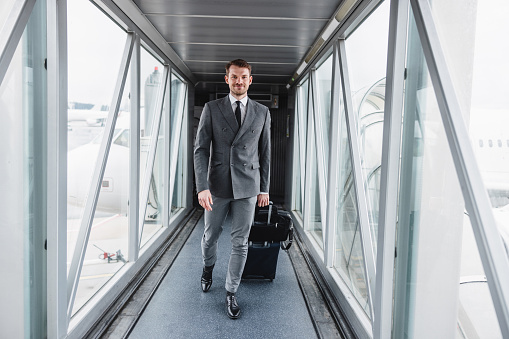 Portrait of a Caucasian man in a suit boarding a plane, smiling for the camera.