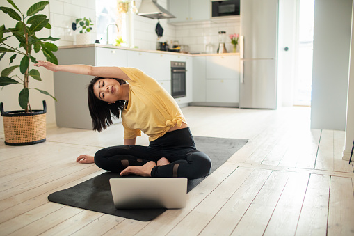 Close up of a young Asian woman stretching and doing yoga at home