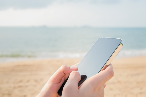 Hand using smartphone on the beach, Summer vacation concept.