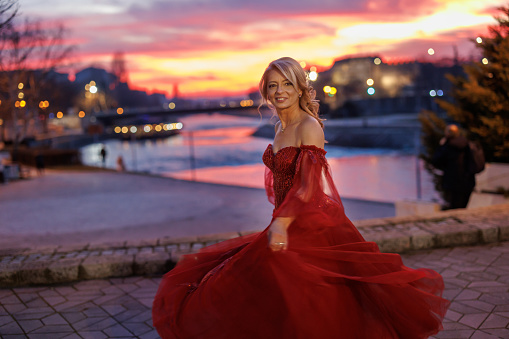 Beautiful mature woman dancing on city quay with beautiful sunset and city lights in background