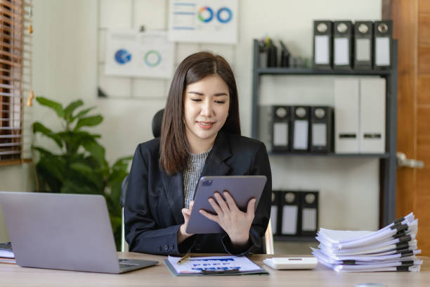 istock Pretty asian businesswoman using laptop and calculator finance graph document for doing financial mathematics on table, report, accounting, statistics and analytical research concept in office 1486703201