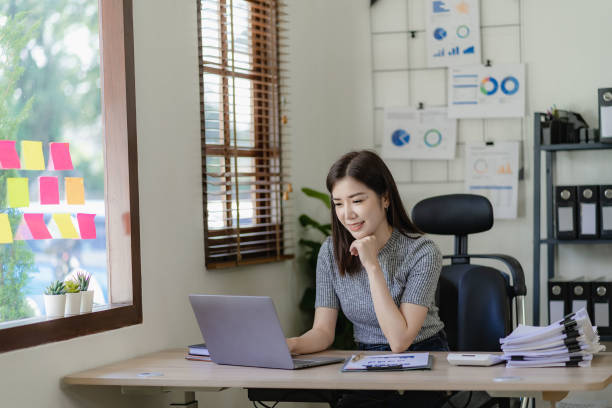 istock Pretty asian businesswoman using laptop and calculator finance graph document for doing financial mathematics on table, report, accounting, statistics and analytical research concept in office 1486703217