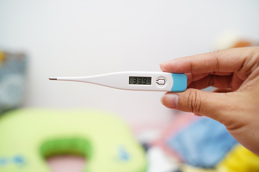 Male hand holding thermometer in hand against bedroom background.