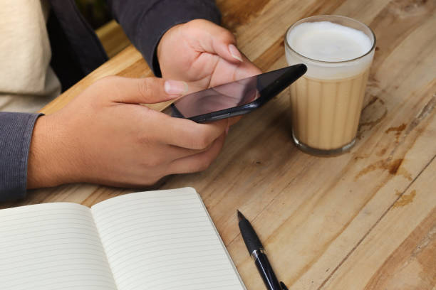 istock Close up of male hand using mobile phone with empty notebook and a cup of coffee while sitting at cafe 1486704676