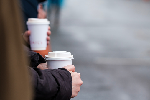 Hands of unrecognizable people are holding cup of coffee in London Marathon. Raining day, warm break concept.