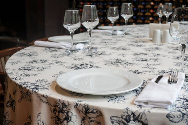 istock Elegant table appointments with white napkin. board set at restaurant on wine bottles shelf background. set in an restaurant. served desk with white tablecloth. white plates, wine glass, fork, knife 1486711255