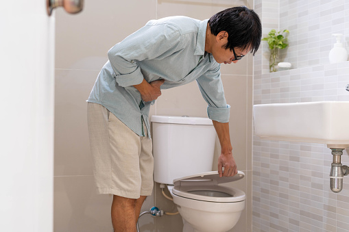 Los hombres están parados frente a la puerta del baño usando sus manos para sostener el abdomen con dolor abdominal severo o diarrea. El concepto de calambres estomacales, diarrea photo