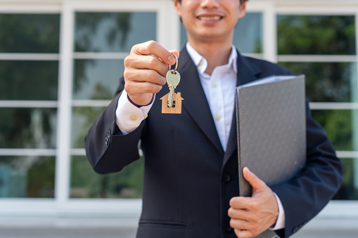 A businessman or home sales agent is happily handing the house keys to a new landlord. New house move ideas, home leasing and selling home.