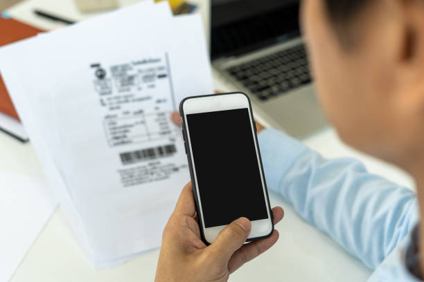 istock hand holding smart phone to scan QR code from invoice on papers for the bills. Scan, bar code online bill payment concept 1486716669