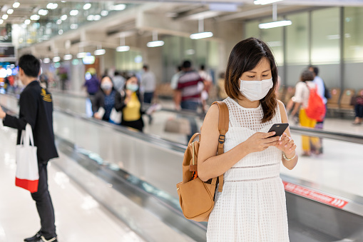 A young Asian woman wearing a mask at the airport is on way to get to the plane at the gate. Travel during the COVIT-19 epidemic