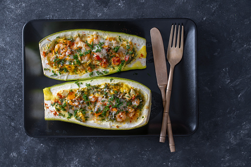Zucchini stuffed with shrimps, vegetables and cheese. Baked zucchini boats, top view, close up