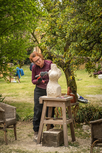 Sebastiano da Po, Italy - April 12 2023: Woman carving a stone during an outdoor sculpture lesson or class in the botanical garden of San Sebastiano da Po Castle near Torino, Piemonte region, Italy