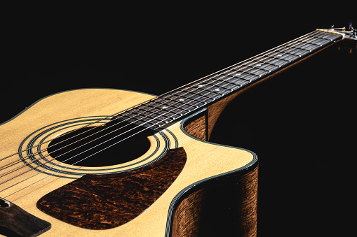 Close up of a classical light guitar on a black background, low key.
