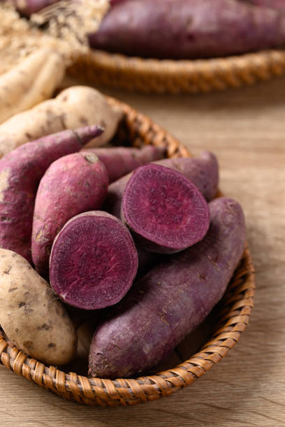 Organic purple sweet potatoes in basket on wooden background stock photo