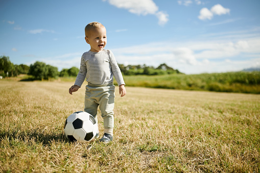 Soccer, sports and baby with ball in field for playing, having fun and adventure in countryside. Childhood, fitness and happy boy outdoors for games on holiday, summer vacation and weekend in nature