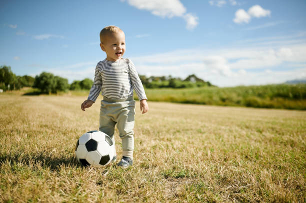 Soccer, sports and baby with ball in field for playing, having fun and adventure in countryside. Childhood, fitness and happy boy outdoors for games for learning, football and weekend in nature stock photo