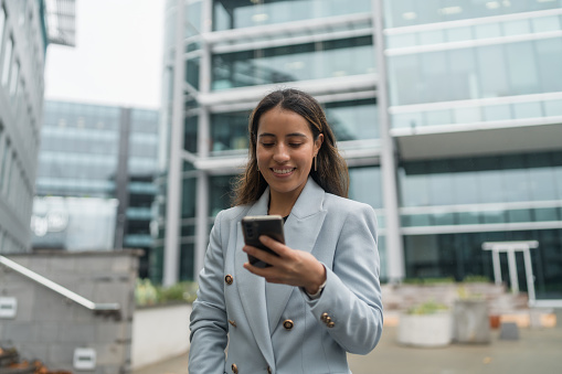 Confident businesswoman using smartphone standing outside office building.