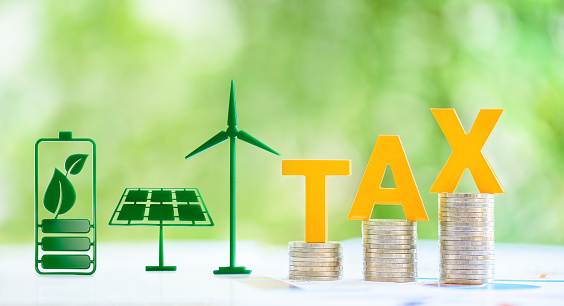 Clean, renewable energy or electricity production tax credits and incentives, financial concept : Green energy symbols e.g solar panel, wind turbine, fuel cell battery and the word TAX atop con stack.