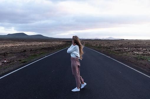 Rear view of blonde woman standing in the middle of the road on sunset dusk, canary islands