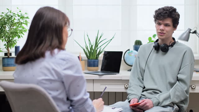 Woman social worker, mentor interviewing, talking to young male in office