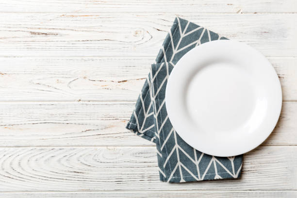 istock Top view on colored background empty round white plate on tablecloth for food. Empty dish on napkin with space for your design 1486737320