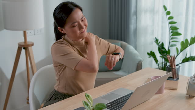 Asian woman working on laptop feels pain from office syndrome sitting at home office.