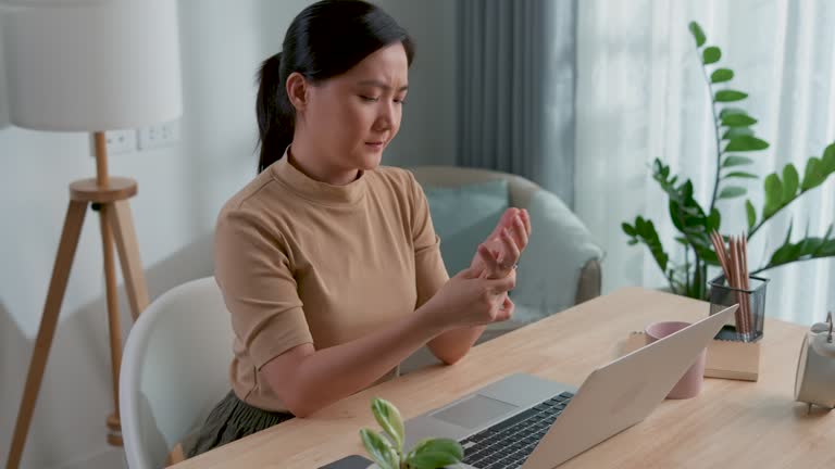 Asian woman working with laptop feel sick suffering from hand pain sitting at home office.