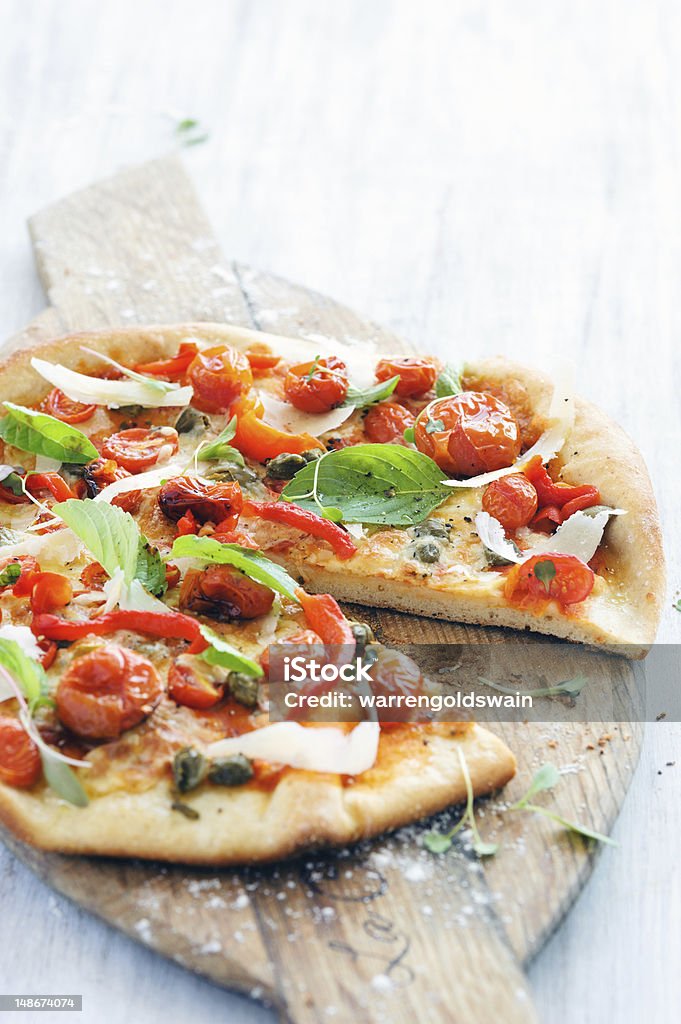 Healthy roasted Italian tomato pizza Fresh, handmade pizza with oven roasted tomatoes, peppers, capers, basil and shaved cheese on rustic wooden board Baked Stock Photo