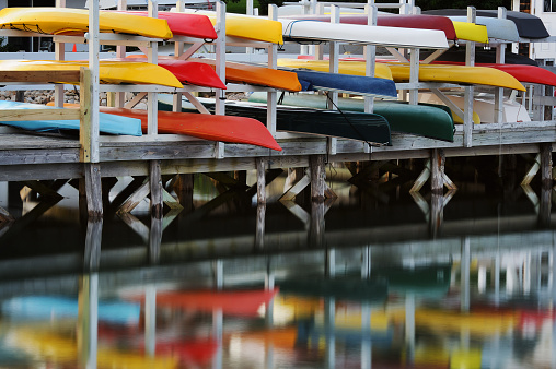 Colorful kayaks and canoes on a boat rack with reflection in calm water