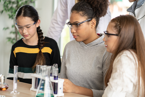 Students in science class doing chemical experiment in laboratory. Girl mixing chemistry in test tube. learning and education concept. Teacher watching and supporting kids