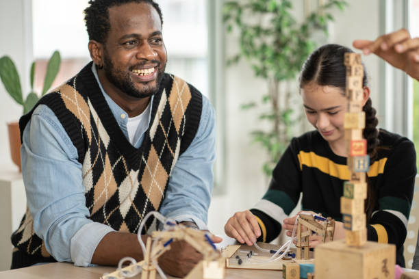 教室で木のおもちゃを並べる生徒を見ている笑顔のアフリカ系アメリカ人教師 - child group of people multi ethnic group classroom ストックフォトと画像