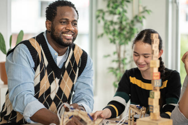 教室で木のおもちゃを並べる生徒を見ている笑顔のアフリカ系アメリカ人教師 - child group of people multi ethnic group classroom ストックフォトと画像