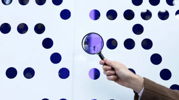 hand holding a magnifying glass in front of a hole of purple light