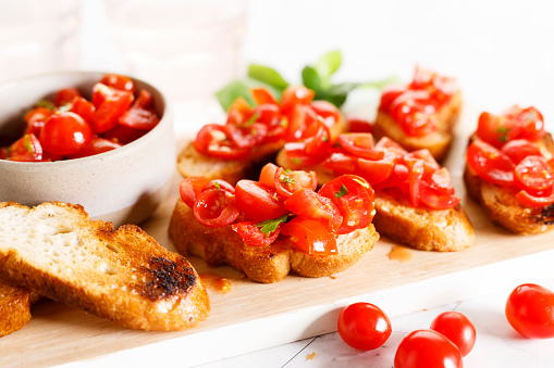 Delicious savory Italian tomato bruschetta slices on white wooden board. Tomato bruschetta with chopped tomatoes, garlic and herbs on toasted bread.