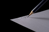 A pencil writing the word love on a white paper