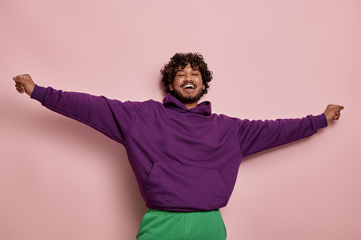 Excited young Indian man looking at camera and gesturing against pink background