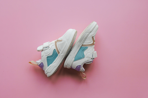 White children's sneakers on a pink background with copy space. Banner.