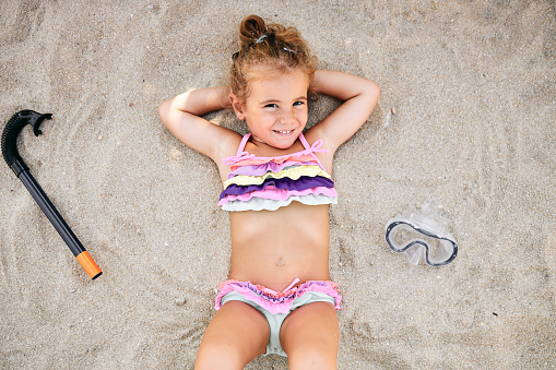 Beautiful girl enjoying sunny day. She is laying down on the sand, happy, smiling, relaxing.