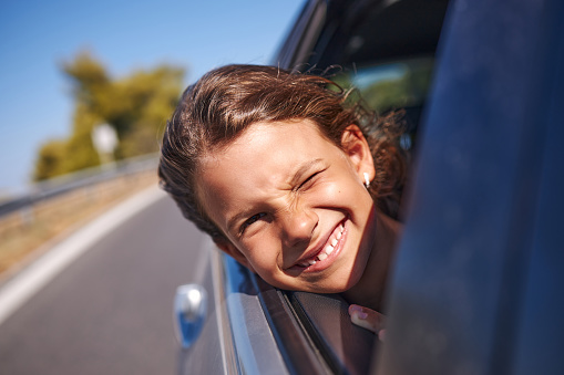 Young girl enjoying road trip while leaning on a car window.