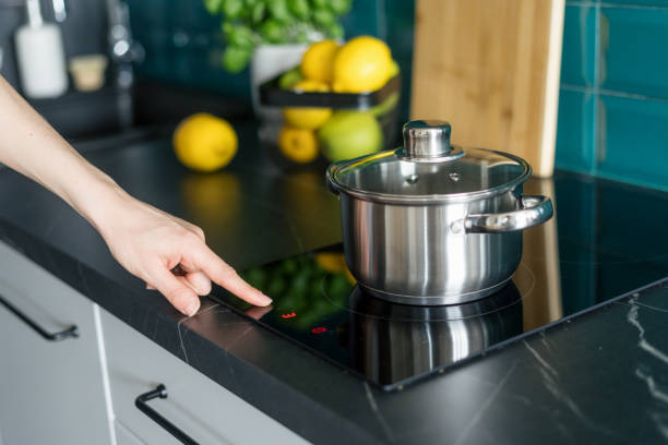 woman turn on electrical stove in modern kitchen cropped shot of female hand press button on induction hob and choose temperature on control panel for cooking dinner in saucepan at home kitchen with stylish interior glass ceramic stove top stock pictures, royalty-free photos & images