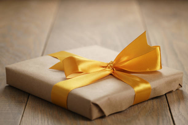 rustic craft paper gift box with orange ribbon bow on wood table, shallow focus