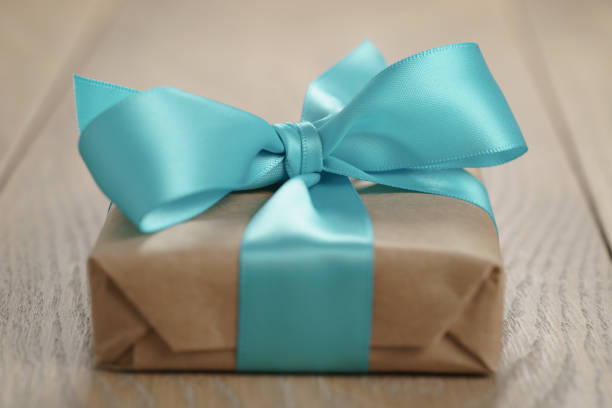 rustic craft paper gift box with blue ribbon bow on wood table, shallow focus