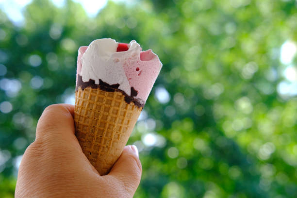 female hand close-up holds, going eat cold ice cream cone, strawberry dessert with fruit jam and chocolate, appetizing eating, happy childhood concept, children's delicacy, healthy and unhealthy food
