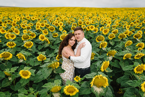 Man and woman hugging, enjoying glade, embrace in nature. Couple hugs in sunflowers field. Honeymoon trip. Weekend vacation holidays concept. Love story on summer day. Selective focus. Romantic moment